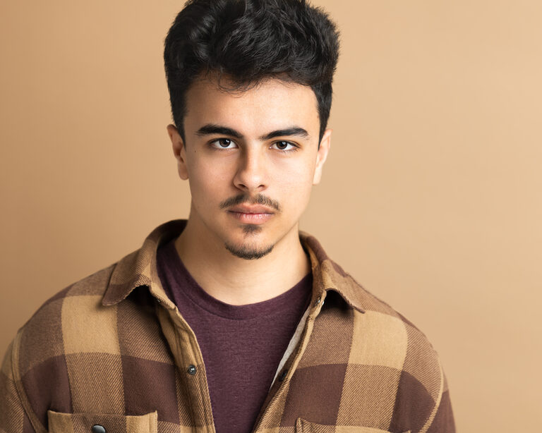 Cyrus Mooney headshot 1, a head-and-shoulders portrait against a warm tan backdrop.